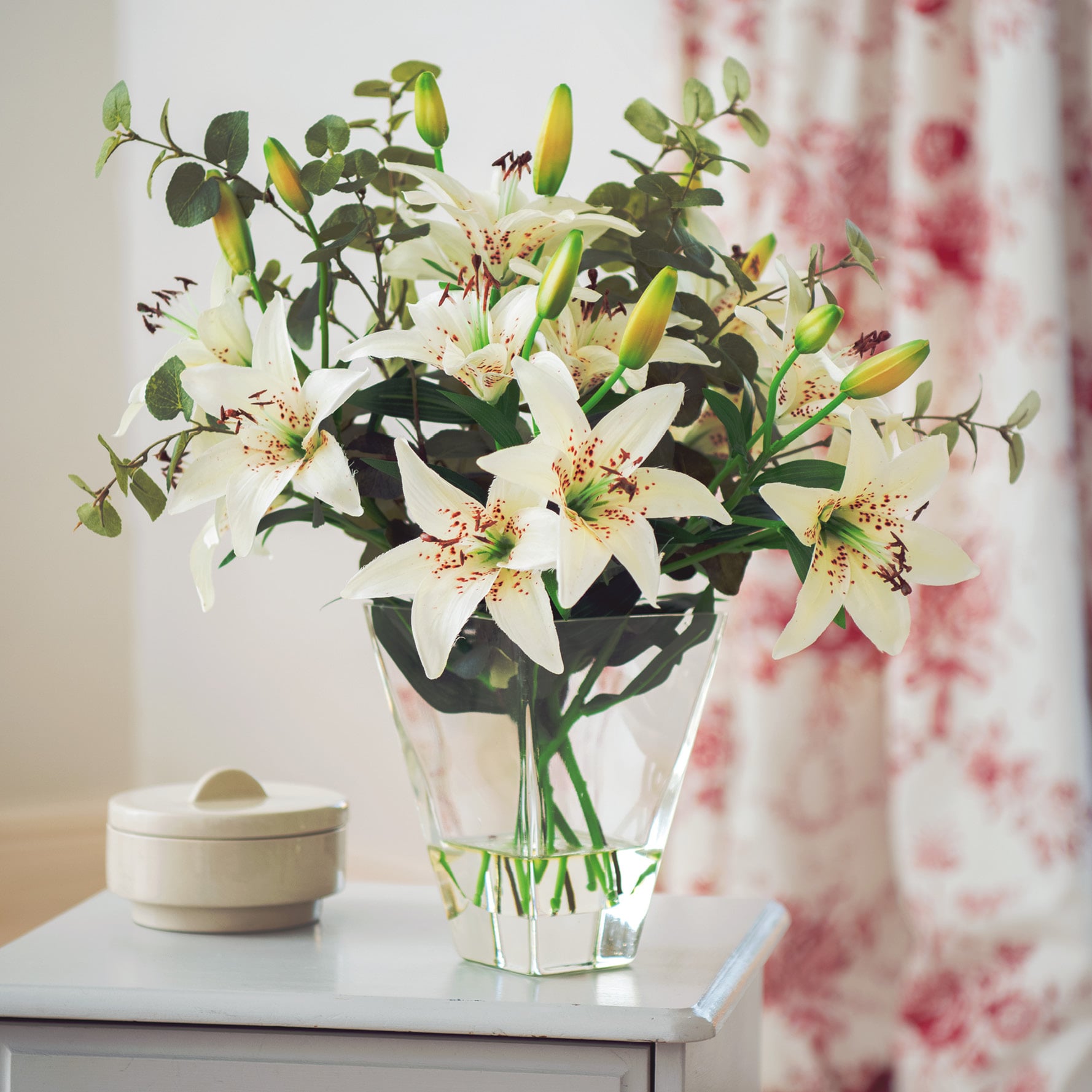 White faux lilies and eucalyptus in clear vase