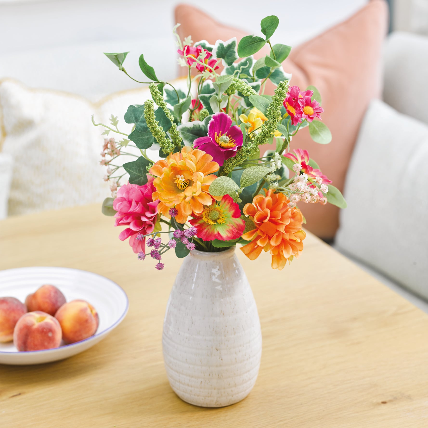 Bright multi-coloured faux Summer flowers in white vase